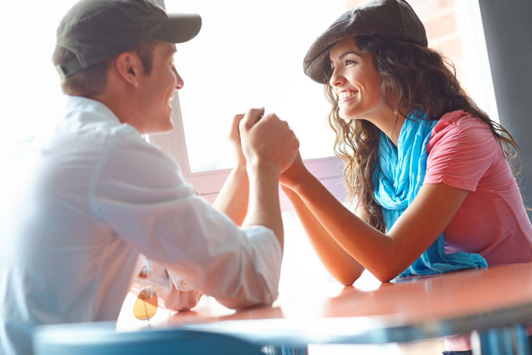 Smiling couple holding hands across a table, expressing connection and affection through love languages for intimacy.