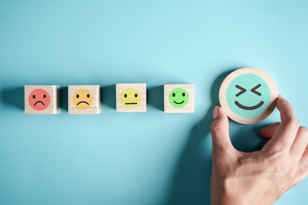 Hand picking the happiest face from a row of emotion blocks, symbolizing tips to boost mental wellbeing.