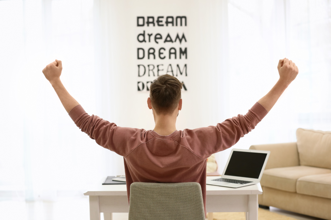 7 Ways to Build AI Passive Income Streams That Actually Work A person raising their arms in celebration at a home desk with a laptop, symbolising success and financial freedom through AI passive income.