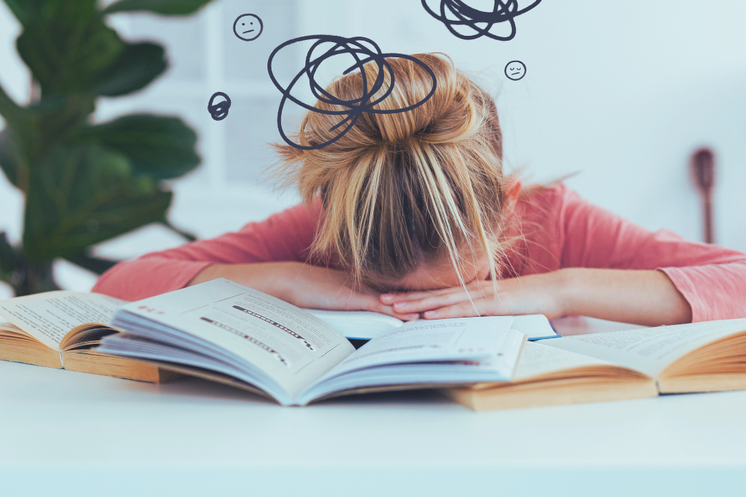 Exhausted person with head down on desk surrounded by books with scribbled lines overhead representing burnout and mental exhaustion