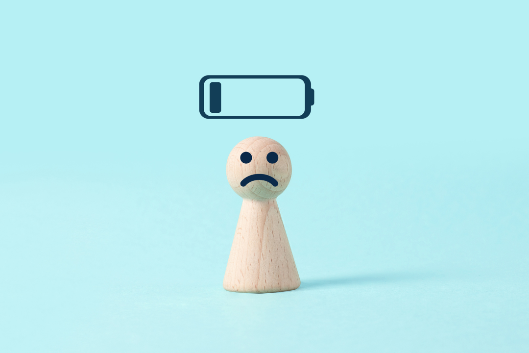 15 Hidden Signs Your Body Is Under Too Much Stress Sad wooden figure with low battery icon above representing physical and mental stress symptoms and exhaustion